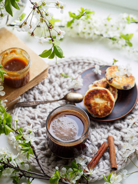 Весенний завтрак на подоконнике. Сладкие чизкейки и чашку кофе. Цветущие ветви белой вишни - Фото, изображение