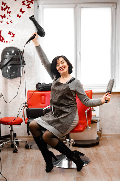 黒髪の女性の美容師が美容師の椅子に腰を下ろして笑いながら - 写真・画像