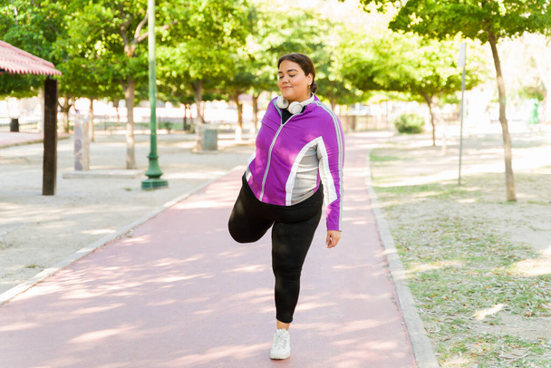 Hermosa mujer de gran tamaño estirando sus piernas antes de un entrenamiento cardiovascular al aire libre. Mujer en forma feliz ejercicio  - Foto, imagen