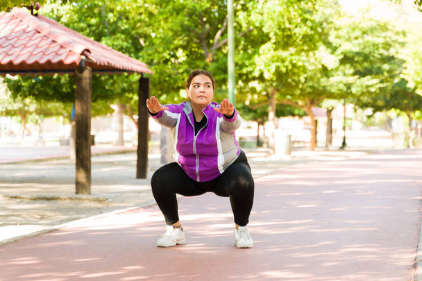 Hispanic woman in her 20s doing squats at the park. Beautiful fat woman reaching her fitness goals - Photo, Image