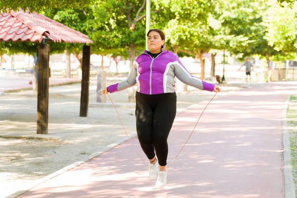 Активная латиноамериканка прыгает по веревке в парке. Толстая женщина сжигает калории, чтобы похудеть  - Фото, изображение