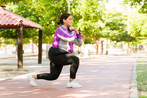 Игривая молодая женщина делает выпады во время тренировки на открытом воздухе. Плюс размер женщины сжигания калорий, чтобы потерять жир и вес - Фото, изображение