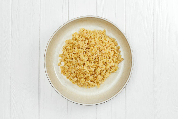 Dietary bulgur in a plate on a white wooden background - Foto, Imagem