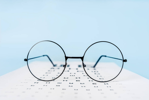 Rusça görüşü kontrol etmek için bir masa, açık mavi arka planda gözlükler ve lensler. Optalmoloji kliniği ya da optik satış konsepti - Fotoğraf, Görsel