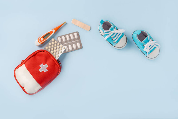 子供用の靴と青い背景に温度計と丸薬付きの応急処置キット。テキスト用のスペース。子供の健康、治療の概念 - 写真・画像