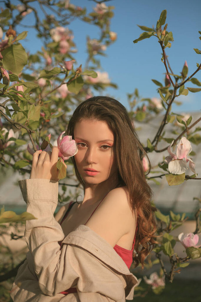 Voorjaarsontwerp met mooie vrouw. Mooie vrouw gezicht met magnolia. Schoonheid sensueel meisje met bloemen. Voorjaarsbloesem achtergrond. vrouw in bloeiende tuin. Dromend jong model tussen magnolia  - Foto, afbeelding