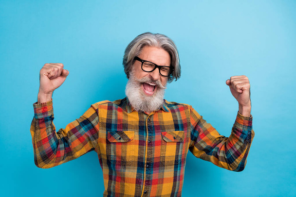Photo of astonished senior man celebrate luck victory champion awesome fists hands isolated over blue color background - Foto, imagen