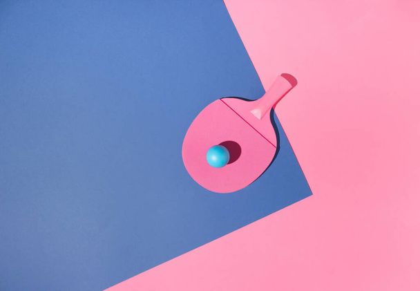 A pink table tennis racket with a blue tennis ball on a blue and a pink background. Minimal concept. - Photo, Image