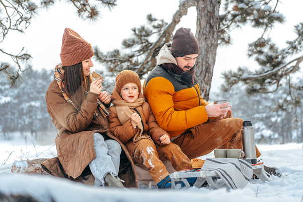 Happy family with cups of hot tea spending time together in winter forest - Foto, afbeelding