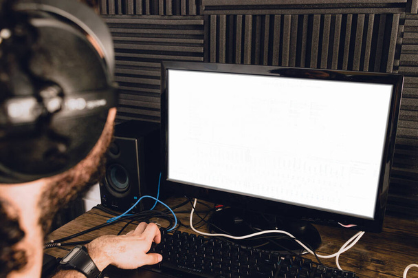 rear view of young caucasian man with headphones using his computer mixing and composing music in his home studio. - Photo, Image