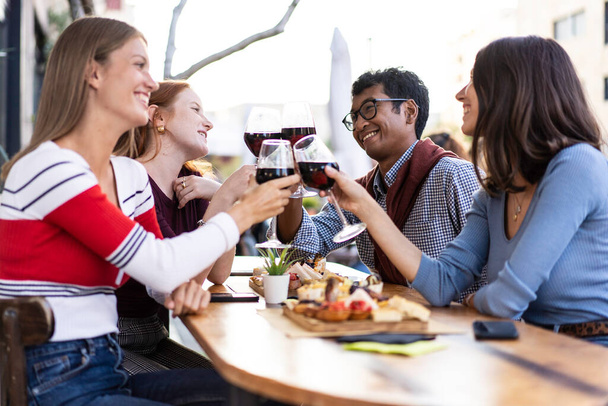 Amis multiraciaux griller du vin rouge au pub en plein air - concept de style de vie alimentaire et de boissons avec des gens heureux s'amusant ensemble au pub - Filtre lumineux avec un accent sur les gars en arrière-plan - Photo, image