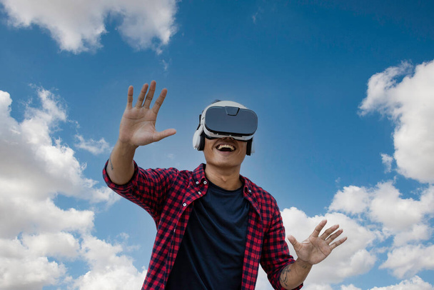 Azjatyccy młodzi faceci bawiący się okularami vr przeciwko błękitnemu niebu i chmurom - azjatycki wpływ społeczny bawiący się nowymi trendami możliwości technologiczne - Gra i koncepcja rzeczywistości wirtualnej - Zdjęcie, obraz