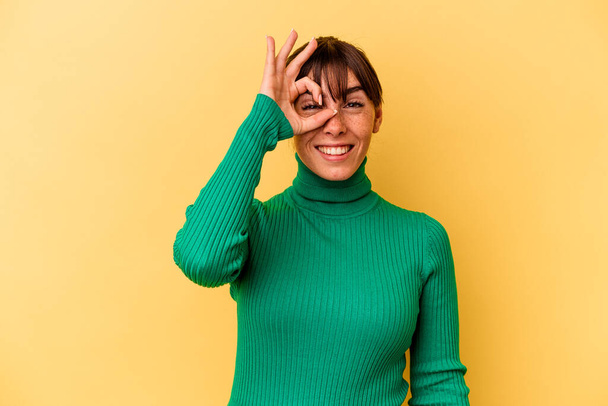 Young Argentinian woman isolated on yellow background excited keeping ok gesture on eye. - Фото, изображение