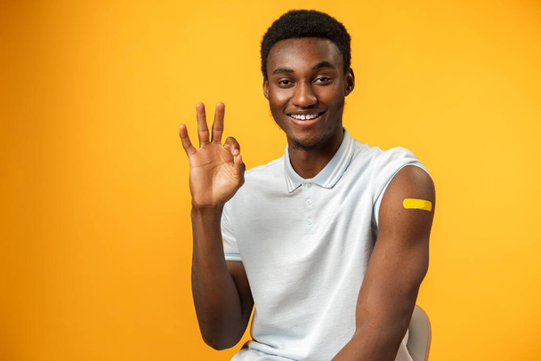 Vaccinated african american man showing his arm against yellow background - Zdjęcie, obraz