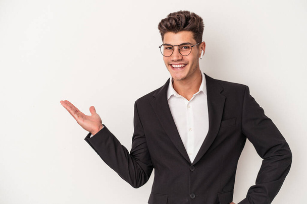 Молодой кавказский бизнесмен в наушниках на белом фоне показывает пространство для копирования на ладони и держит другую руку на талии. - Фото, изображение
