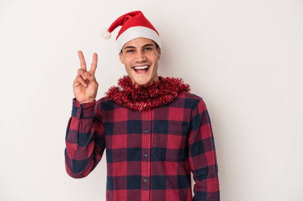 Young caucasian man celebrating Christmas isolated on white background joyful and carefree showing a peace symbol with fingers. - Fotoğraf, Görsel