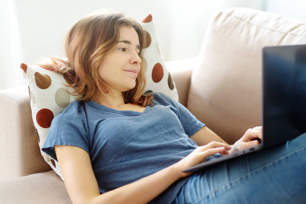 Young woman working with laptop computer lying on sofa at home. Freelancer or blogger. Distance learning of new profession. Additional education. Retraining courses. Online business. Business woman. - Фото, изображение