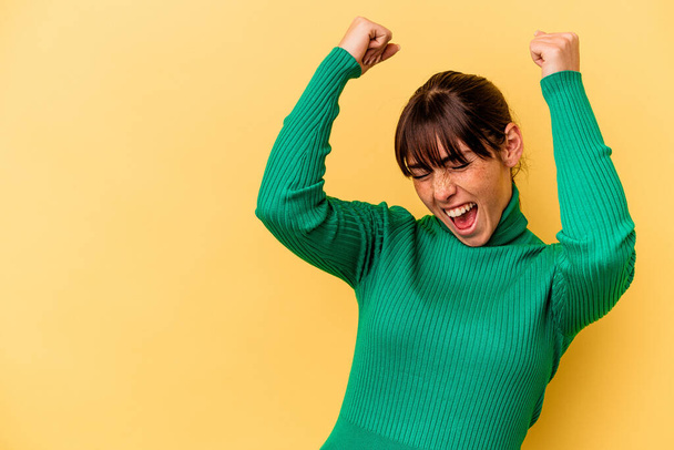 Young Argentinian woman isolated on yellow background raising fist after a victory, winner concept. - Фото, изображение