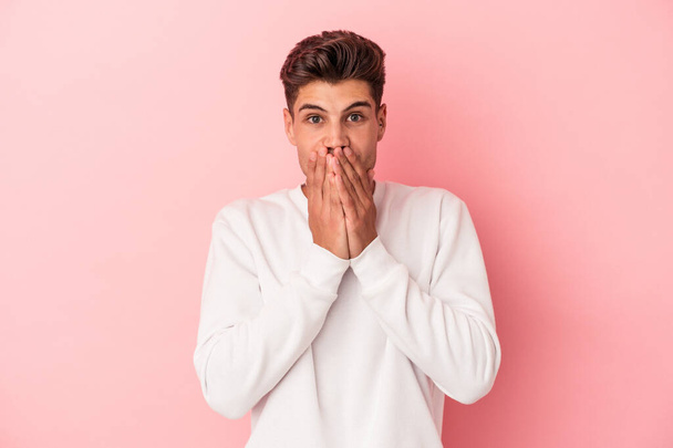 Junger kaukasischer Mann isoliert auf rosa Hintergrund schockiert Mund mit Händen bedecken. - Foto, Bild