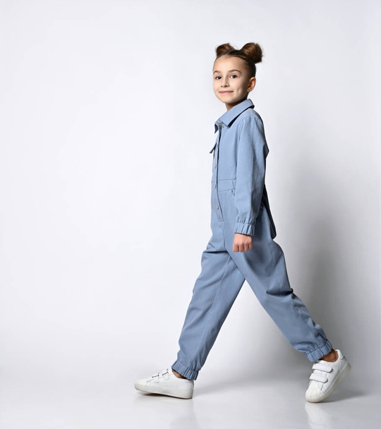 beautiful girl with a bagel hairstyle walking in a blue cotton summer jumpsuit with comfortable pockets. on a light background. - Fotografie, Obrázek