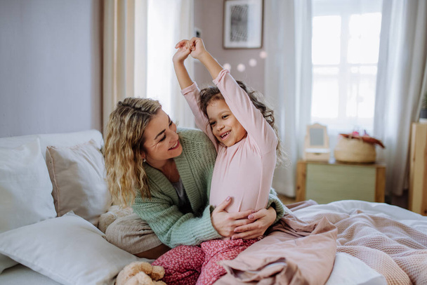 Happy mother hodling her little daughter stretching in bed when waking up in morning. - Φωτογραφία, εικόνα