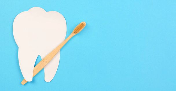 Witte tanden en houten tandenborstel op een blauwe achtergrond. Tandheelkundige zorg concept, banner, kopieerruimte - Foto, afbeelding