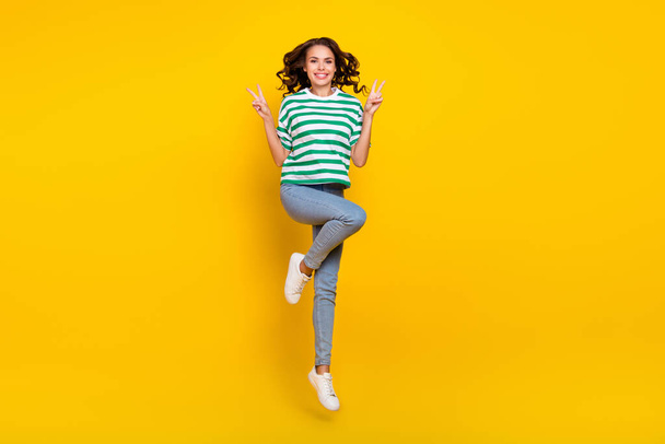 Full body photo of young cheerful girl have fun show fingers peace v-symbol jump isolated over yellow color background - Foto, immagini