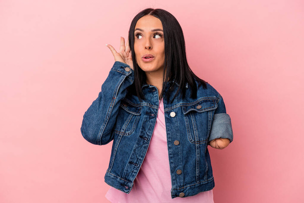 Young caucasian woman with one arm isolated on pink background trying to listening a gossip. - Photo, Image