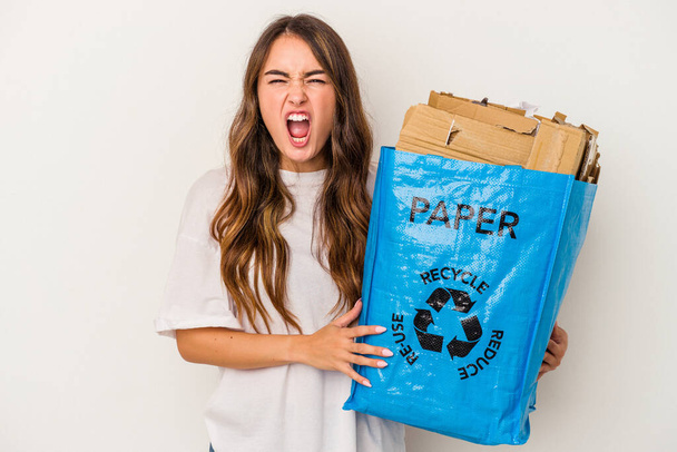 Young caucasian woman recycling paper isolated on white background screaming very angry and aggressive. - Foto, Imagem