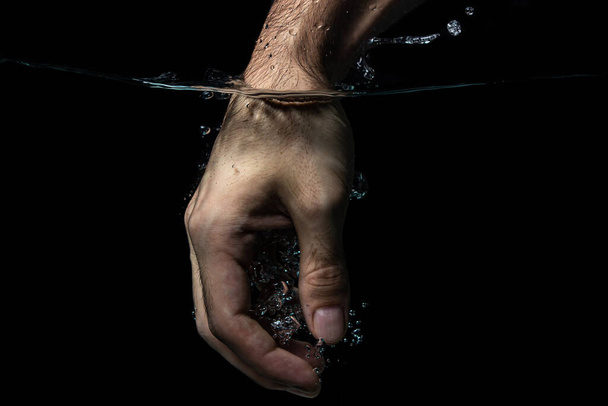 The hand is immersed in water on a black background. Clean and transparent water. hand washing - 写真・画像