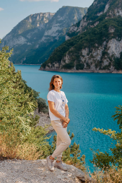 Girl tourist stands on the shore of a lake in the mountains. beautiful landscape, Piva Lake in Montenegro.. Woman is standing on the coast of Piva lake at sunset in summer. Landscape with girl, famous - Foto, immagini