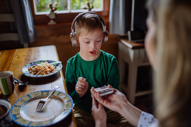 Menino com síndrome de Down com a mãe almoçando e usando smartphone em casa - Foto, Imagem