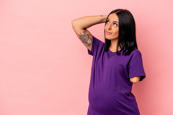 Young pregnant woman with one arm isolated on pink background touching back of head, thinking and making a choice. - Photo, Image