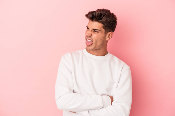 Jonge blanke man geïsoleerd op roze achtergrond grappig en vriendelijk steken uit tong. - Foto, afbeelding