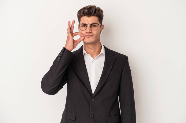 Νεαρός επιχειρηματίας καυκάσιος που φοράει ακουστικά απομονωμένα σε λευκό φόντο με δάχτυλα στα χείλη κρατώντας ένα μυστικό. - Φωτογραφία, εικόνα