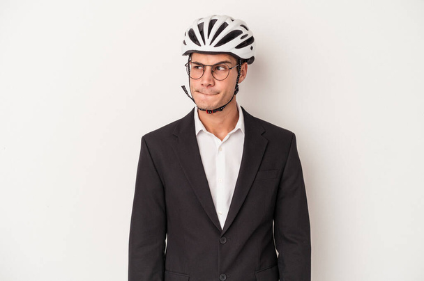 Young business caucasian man holding bike helmet isolated on white background confused, feels doubtful and unsure. - Valokuva, kuva