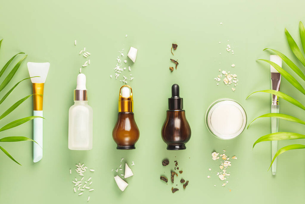 Fermented beauty care. Hande made rice serum, green tea serum, oatmeal cream, coconut water and cosmetic accessories on a green background. Natural homemade cosmetics based on fermented products - Foto, afbeelding