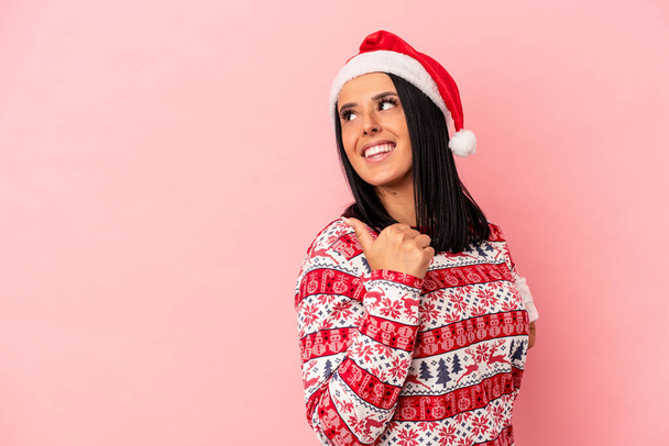Young caucasian woman with one arm celebrating Christmas isolated on pink background points with thumb finger away, laughing and carefree. - Photo, Image
