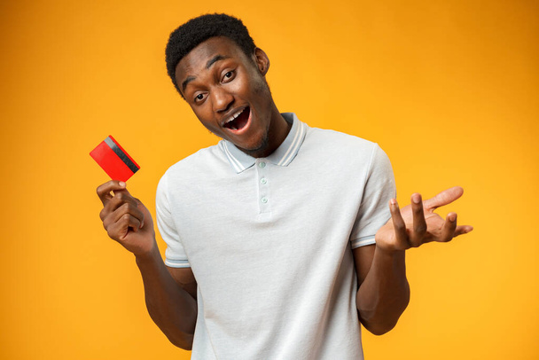 Afro amerykański człowiek trzyma czerwoną kartę kredytową na żółtym tle w studio - Zdjęcie, obraz