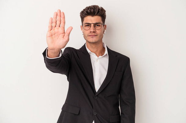 Молодой кавказский бизнесмен в наушниках на белом фоне стоит с протянутой рукой, показывая знак "стоп", препятствуя вам. - Фото, изображение