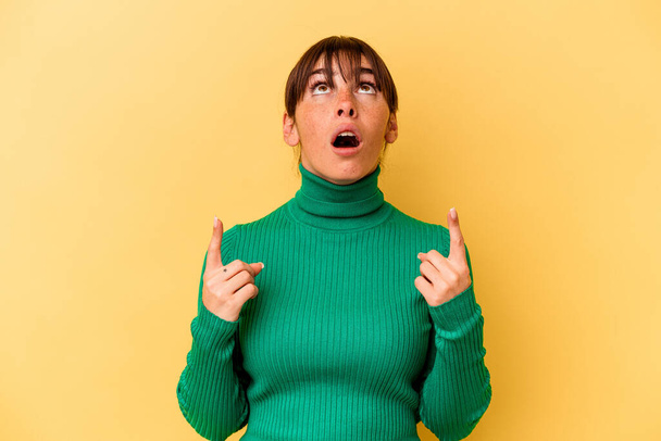 Young Argentinian woman isolated on yellow background pointing upside with opened mouth. - Foto, imagen