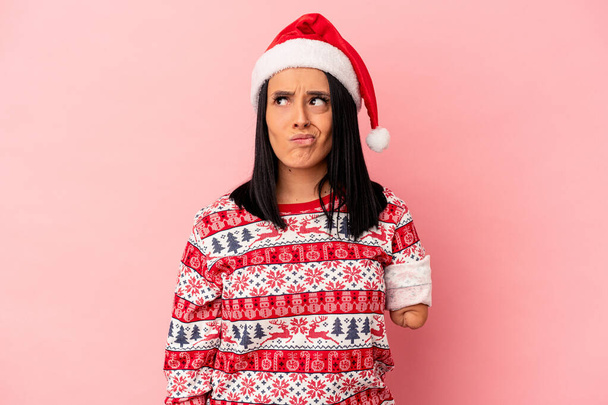 Young caucasian woman with one arm celebrating Christmas isolated on pink background confused, feels doubtful and unsure. - Fotoğraf, Görsel