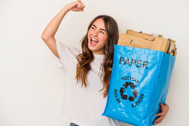 Young caucasian woman recycling paper isolated on white background raising fist after a victory, winner concept. - Foto, Imagem