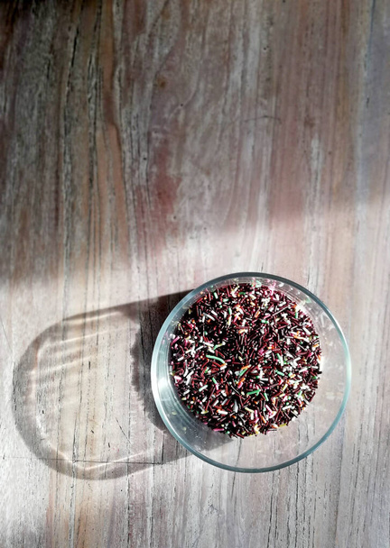 Chocolate granules with many colors,placed on the glass bowl,with wooden table background and shadow - Photo, Image