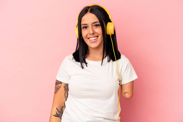 Young caucasian woman with one arm listening to music isolated on pink background happy, smiling and cheerful. - Foto, afbeelding