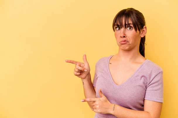 Jonge Argentijnse vrouw geïsoleerd op gele achtergrond geschokt wijzend met wijsvingers naar een kopieerruimte. - Foto, afbeelding