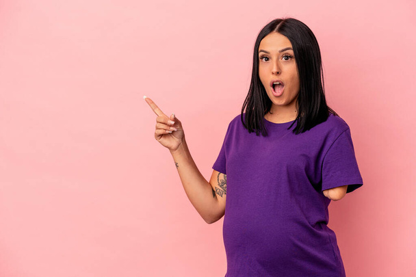 Young pregnant woman with one arm isolated on pink background pointing to the side - Photo, Image