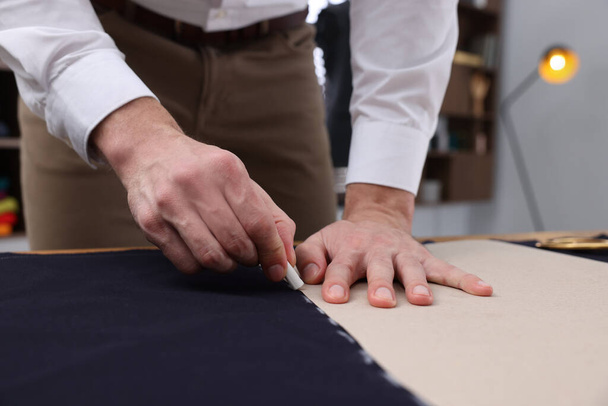 Tailor marking sewing pattern on fabric with chalk at table, closeup - Fotografie, Obrázek