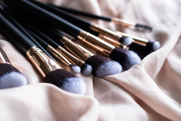 Set de lujosos cepillos de maquillaje negro sobre tela de seda beige - Foto, imagen