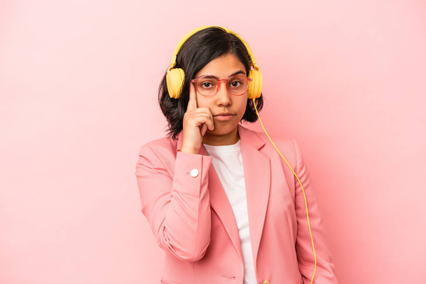 Giovane donna latina che ascolta musica isolata su sfondo rosa puntando tempio con il dito, pensando, focalizzata su un compito. - Foto, immagini